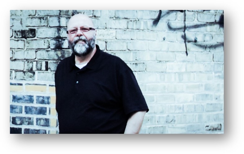 Man in black shirt standing by a brick wall with Graffiti